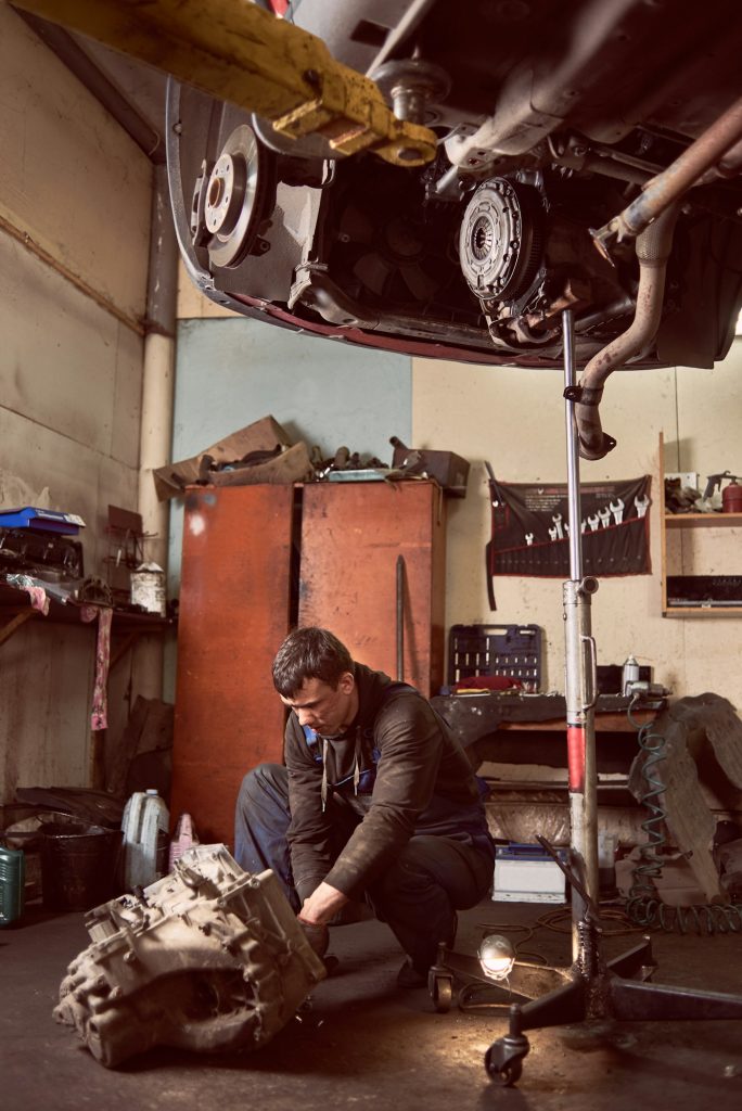 Repair man fixing car at auto repair shop under lifted vehicle